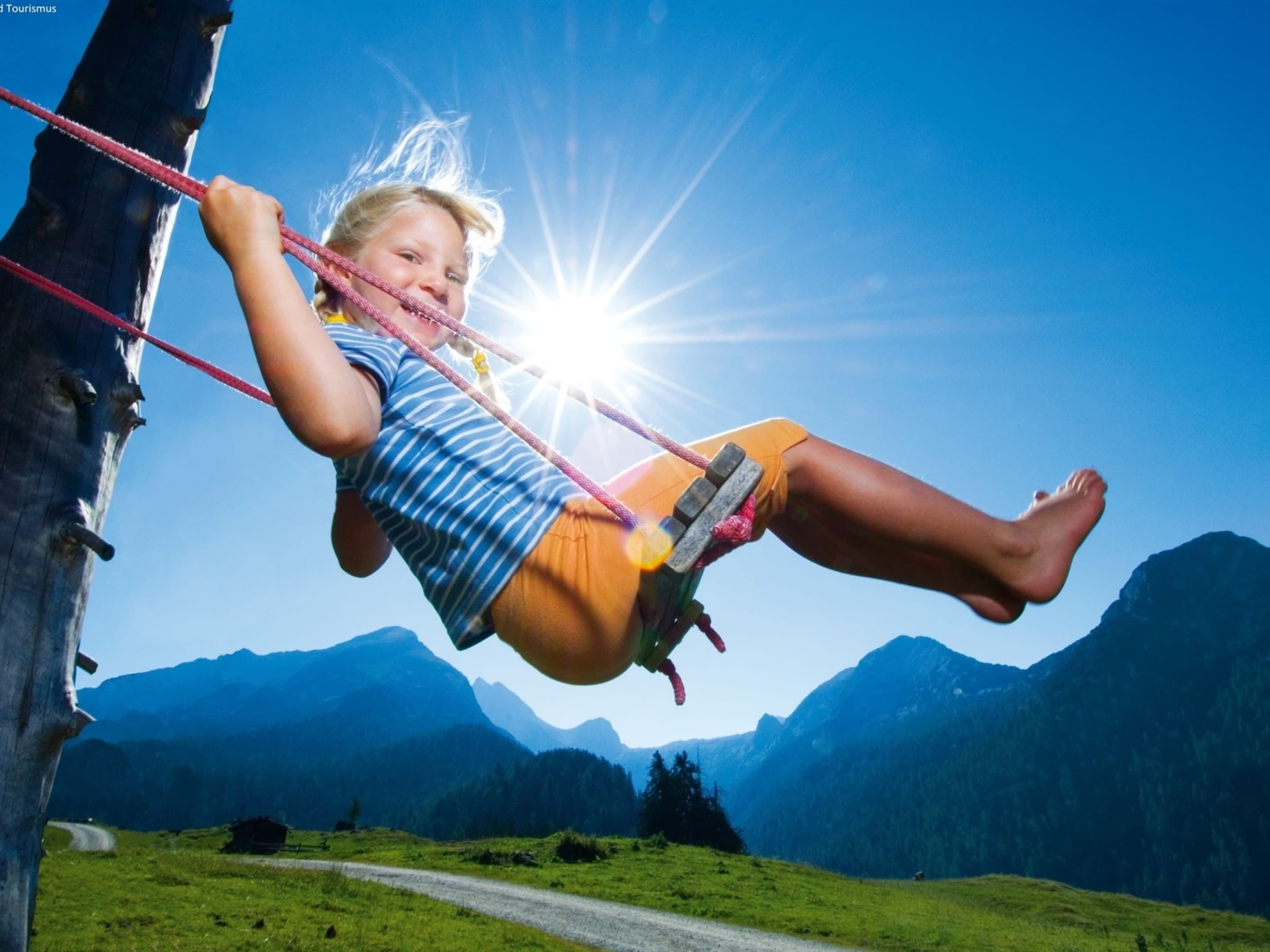 A child on a swing with a mountainous landscape in the background.