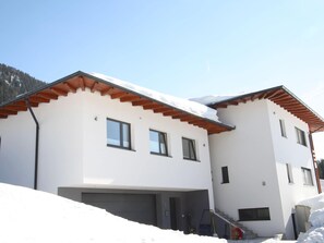 Une maison moderne à deux étages, avec une façade blanche, des poutres de toit en bois et un garage.