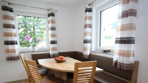 A dining area with a wooden table and chairs, a bench, and a window with curtains. - Apartment in Annaberg Near Dachstein Ski (Annaberg-Lungoetz)