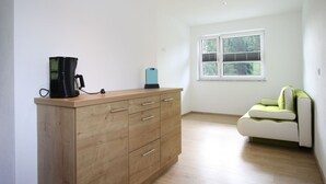 A room with a wooden cabinet, a green and white sofa, a window with blinds, and a black coffee maker. - Apartment in Annaberg Near Dachstein Ski (Annaberg-Lungoetz)