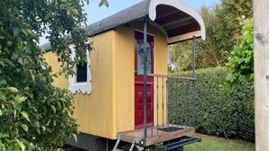 En liten, gulmålad träbyggnad med en röd dörr och en överbyggd veranda.