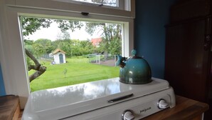 Ett kök med en spis, en vattenkokare och ett fönster med utsikt över en trädgård.