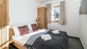 A bedroom with a bed, wooden wardrobe, a window with curtains, and a wall-mounted TV. - Apartment in Hollersbach With Sauna Near ski Area (Hollersbach im Pinzgau)