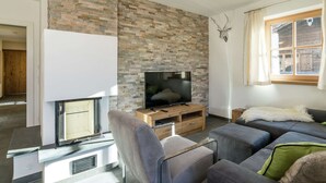 A modern living room with a stone wall, a fireplace, a television, and a sofa. - Apartment in Hollersbach With Sauna Near ski Area (Hollersbach im Pinzgau)