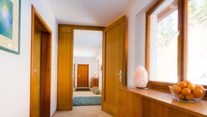 A hallway with wooden doors, a salt lamp, and a bowl of oranges on a windowsill.
