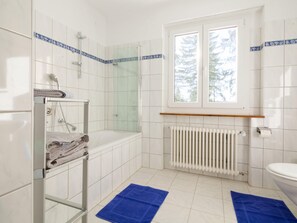 A bathroom with a bathtub, a glass shower enclosure, a toilet, and a window with a view of trees.