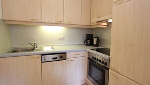 Una cucina compatta con mobili in legno chiaro, lavastoviglie, piano cottura e macchina da caffè.