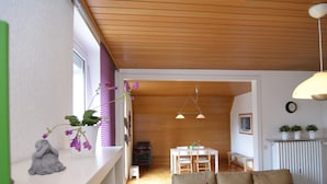 Ein gemütliches Wohnzimmer mit Holzboden, einer Couch, einem Esstisch und einer kleinen Küchenzeile.