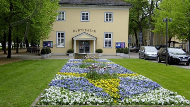 Ein Gebäude mit der Aufschrift „KURTHEATER“ und einem symmetrischen Garten davor.
