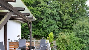 Eine Terrasse im Freien mit einem runden Tisch und vier Stühlen, umgeben von einer Holzhütte und einem üppigen Garten.