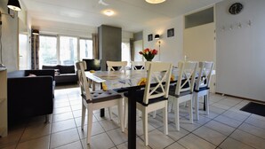 A dining area with a table set for four, surrounded by white chairs, a vase of flowers, and a clock on the wall. - Appealing Holiday Home in Guelders near Forest (Lochem)