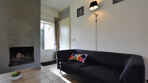 A living room with a dark-colored sofa, a wooden coffee table with a plant, a fireplace, and a door leading outside. - Appealing Holiday Home in Guelders near Forest (Lochem)