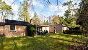 A brick house with a tiled roof, a covered patio with outdoor furniture, and a well-maintained lawn. - Appealing Holiday Home in Guelders near Forest (Lochem)