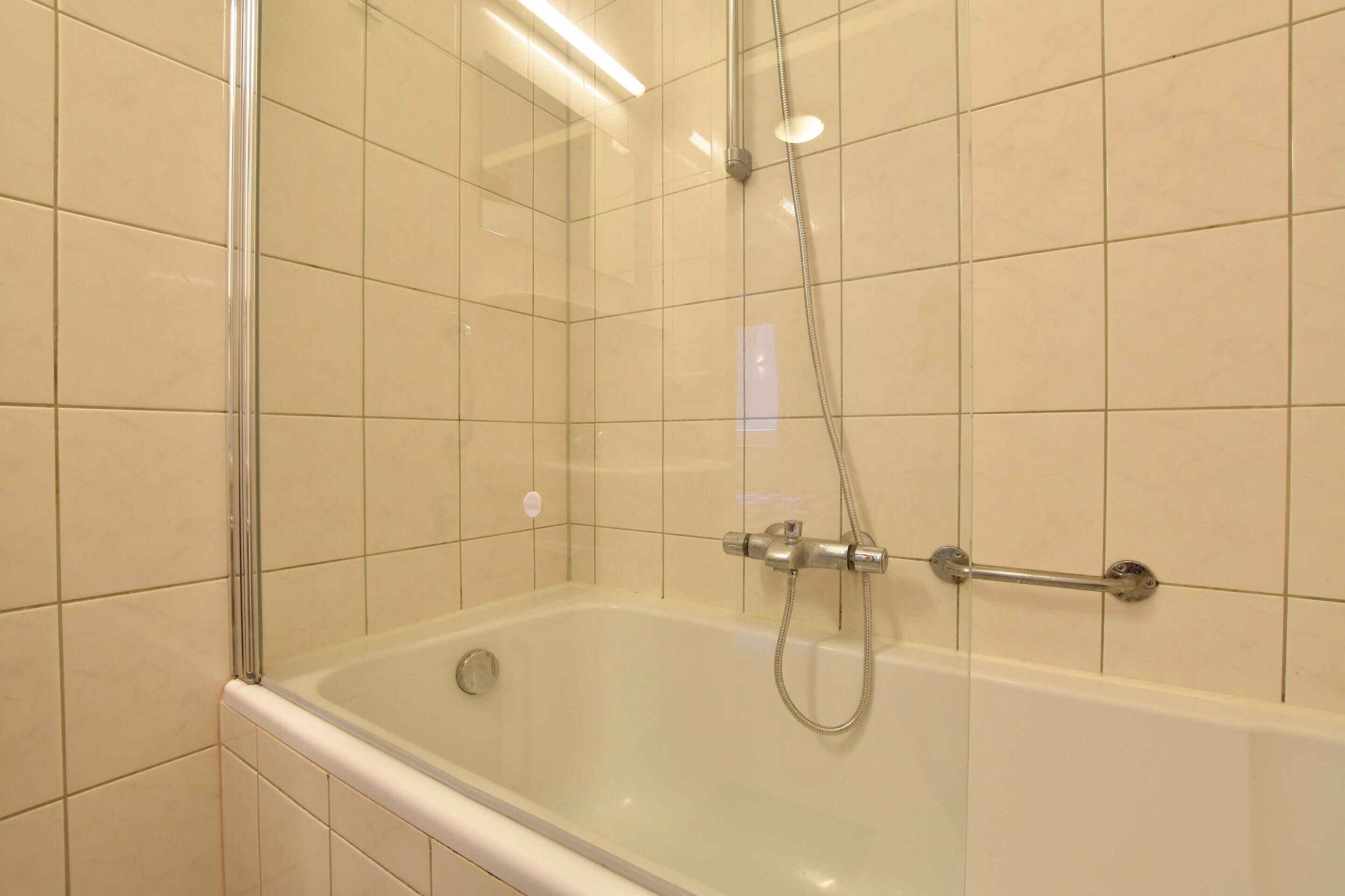Une salle de bain moderne dotée d’une douche à parois de verre, d’un pommeau de douche amovible et d’un robinet mural.