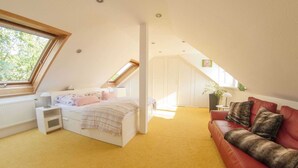 A bedroom with a sloped ceiling, a bed, a red leather sofa, a window, and a skylight. - Holiday Home with Garden & Terrace near Rennsteig in Thuringian Forest (Waltershausen)