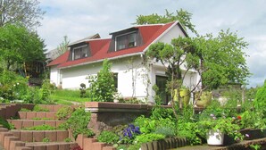 A two-story house with a red roof, surrounded by a garden with various plants and flowers. - Holiday Home with Garden & Terrace near Rennsteig in Thuringian Forest (Waltershausen)