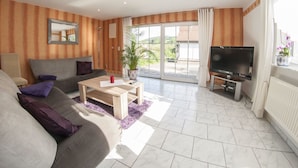 A living room with a sofa, a coffee table, a TV, and a sliding glass door leading to a balcony. - Holiday Home with Garden & Terrace near Rennsteig in Thuringian Forest (Waltershausen)