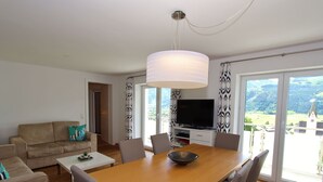 A modern living room with a wooden dining table, grey chairs, a sofa, and a television.