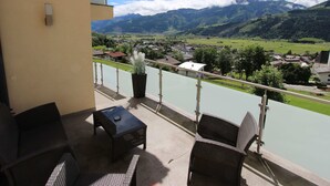 A balcony with wicker furniture, a potted plant, and a view of a river and mountains.