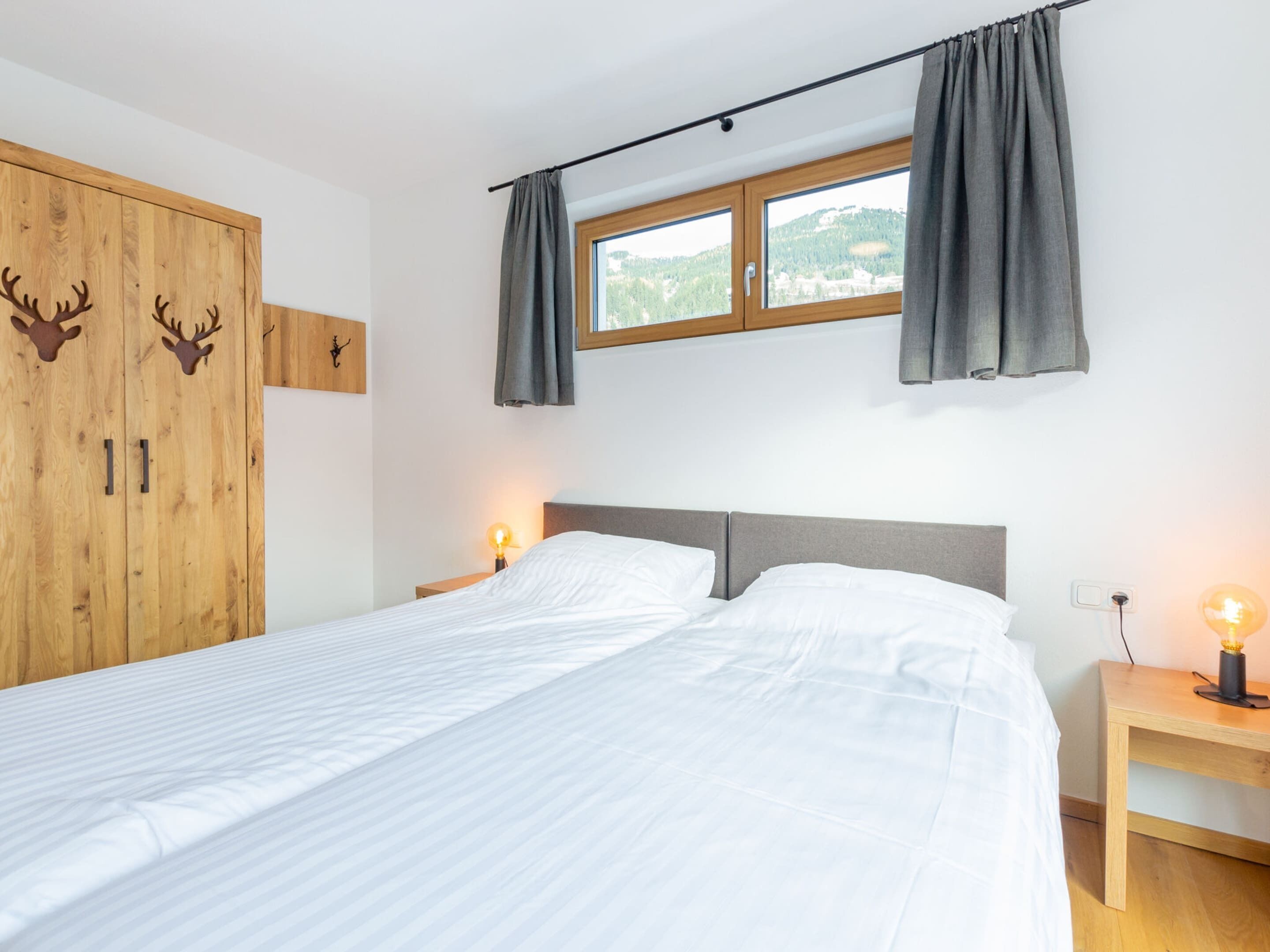 Ein Schlafzimmer mit einem Bett, einem Holzschrank mit Hirschdekorationen, einem Fenster mit Vorhängen und Nachttischlampen.