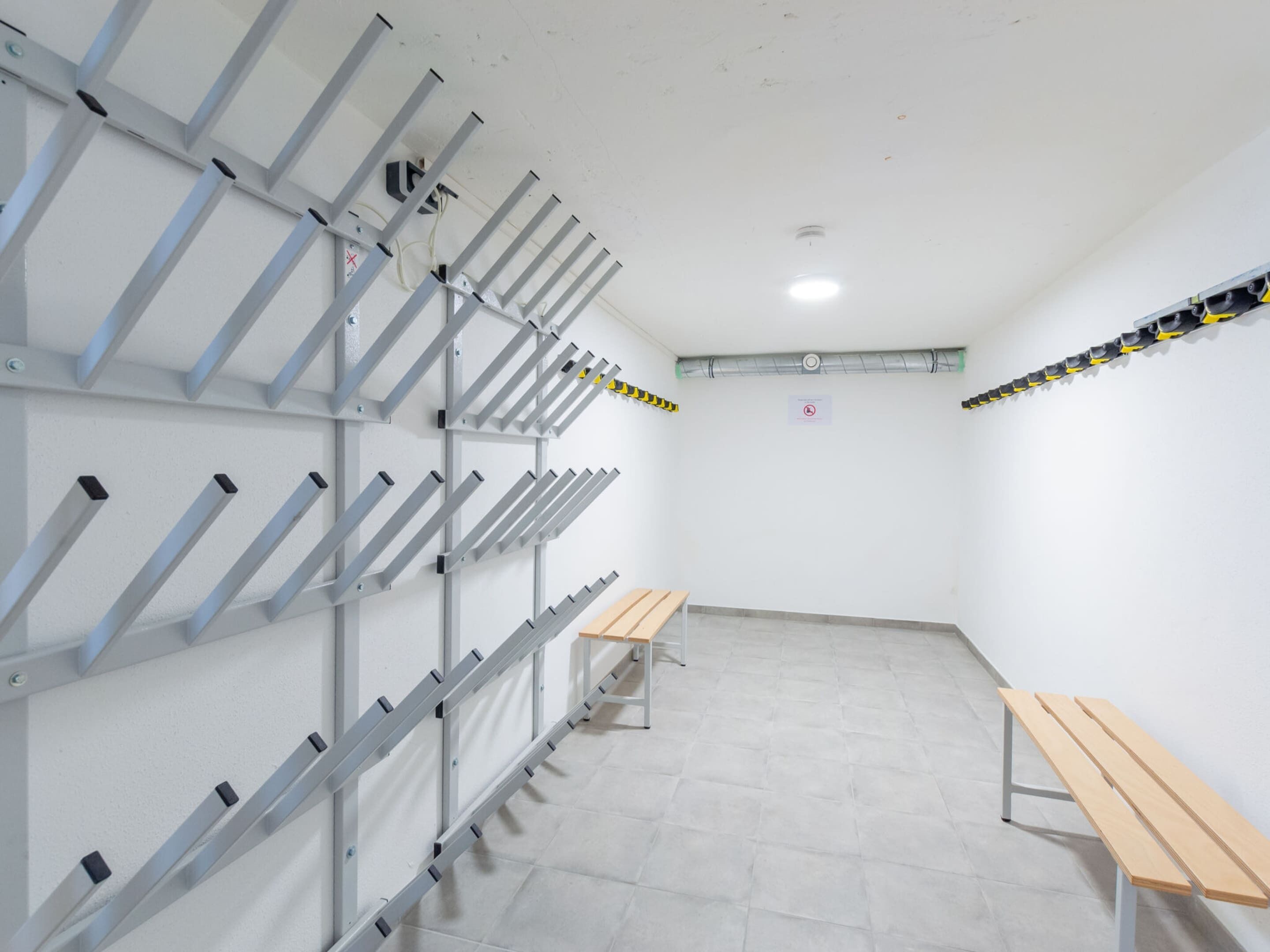 A room with a metal rack system for hanging items, a wooden bench, and a tiled floor.
