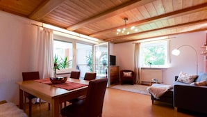 A cozy living room with a wooden dining table, chairs, a sofa, and a TV. - Apartment With Sauna (Zandt)