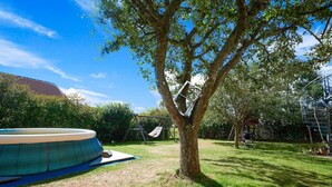 A backyard with a tree, a swing set, and a swimming pool. - Apartment With Sauna (Zandt)