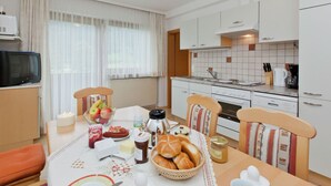 A modern kitchen with white cabinets, a Bosch oven, and a dining area with a table set for breakfast. - Beautiful Apartment With Large, Sunny Balcony (Hollersbach im Pinzgau)