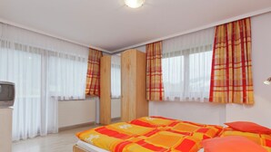 A modern bedroom with a bed, a television, and large windows with curtains. - Beautiful Apartment With Large, Sunny Balcony (Hollersbach im Pinzgau)