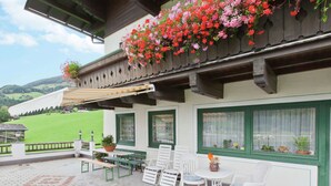 An outdoor patio with a table and chairs, a hanging flower basket, and a view of a green landscape. - Beautiful Apartment With Large, Sunny Balcony (Hollersbach im Pinzgau)