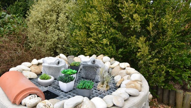 A garden with a circular stone planter surrounded by rocks and potted plants. - Ferienhaus in Saldenburg mit Sauna (Saldenburg)