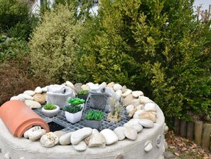 Un jardin avec un jardinière circulaire en pierre, entourée de rochers et de plantes en pot.
