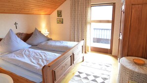 A bedroom with two beds, a wooden ceiling, a window with curtains, a door, and a small table with a bowl. - Ferienhaus in Saldenburg mit Sauna (Saldenburg)