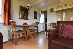 A dining area with a wooden table and chairs, a painting on the wall, and a window with curtains. - Holiday Home in With Cycling Area (Den Ham)