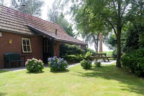 A brick house with a tiled roof, a bench, and a picnic table in a garden with various plants and a large tree. - Holiday Home in With Cycling Area (Den Ham)
