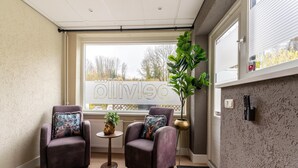 Una habitación moderna con dos sillones de cuero, una pequeña mesa redonda con una planta y un amplio ventanal con vistas a árboles.