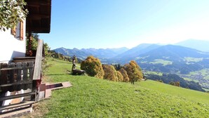 A rustic building with a wooden staircase leading to a balcony overlooking a valley with mountains in the background.