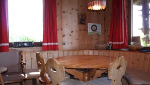 A wooden dining area with a round table and chairs, a radio on the window sill, and a chandelier.