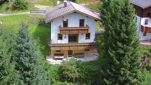 A two-story chalet with a balcony, surrounded by greenery and other buildings. - Boutique Chalet in Maria Alm near Hochkönig (Maria Alm am Steinernen Meer)