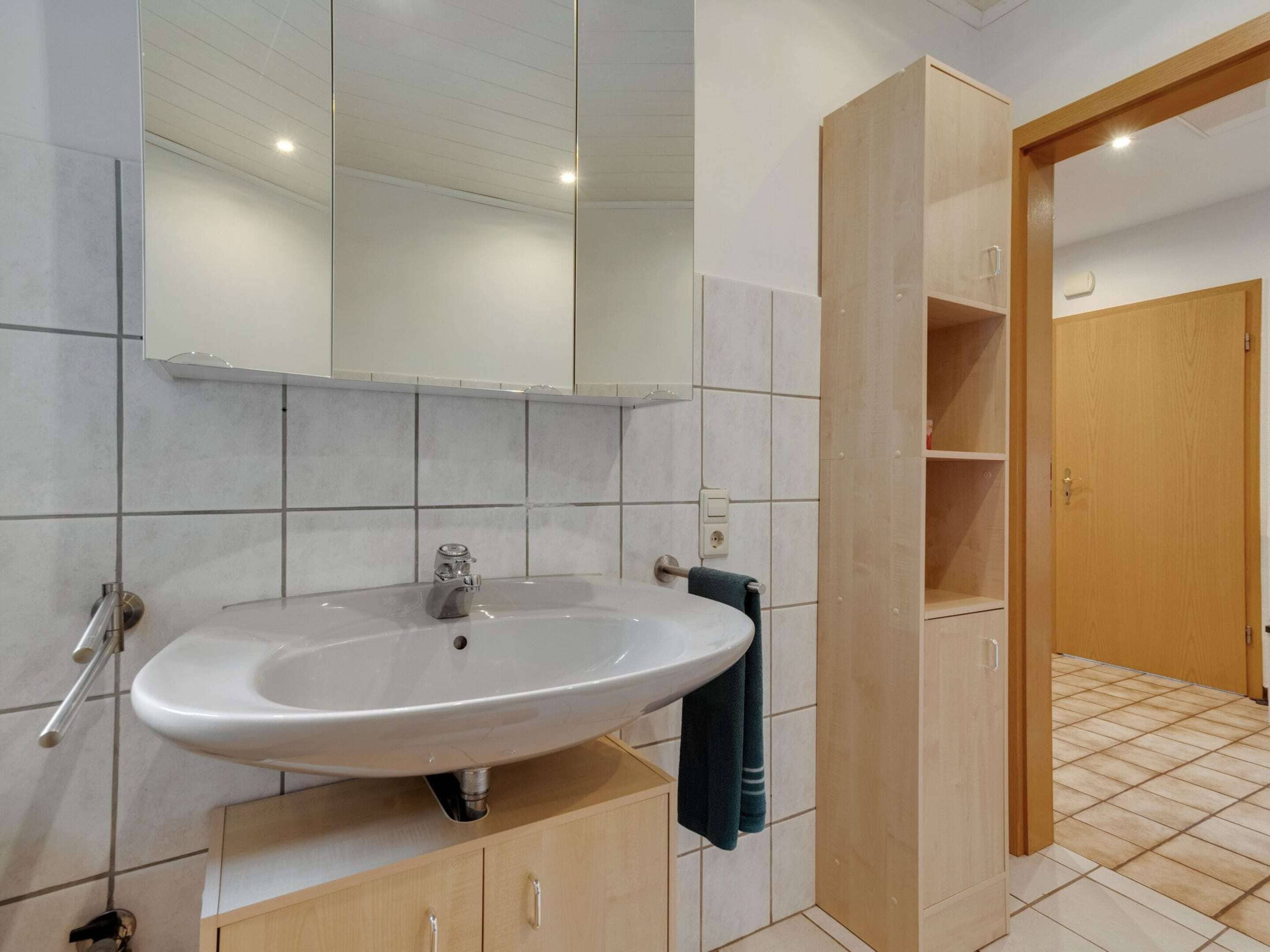 Un baño con un lavamanos blanco, un espejo y un armario de madera.