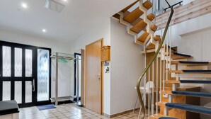 Un interior moderno con una escalera de madera, una puerta de cristal que da a la zona de ducha y un suelo de baldosas.