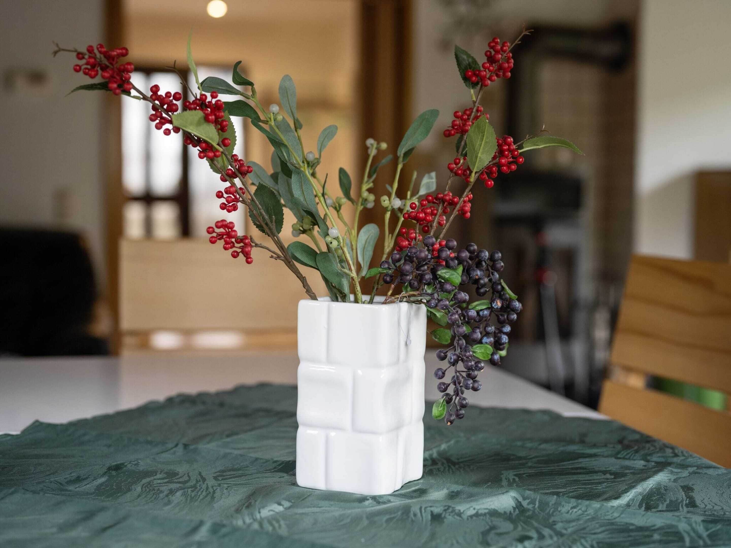 Un vase en céramique blanche orné d’un motif géométrique, posé sur une nappe verte à texture.