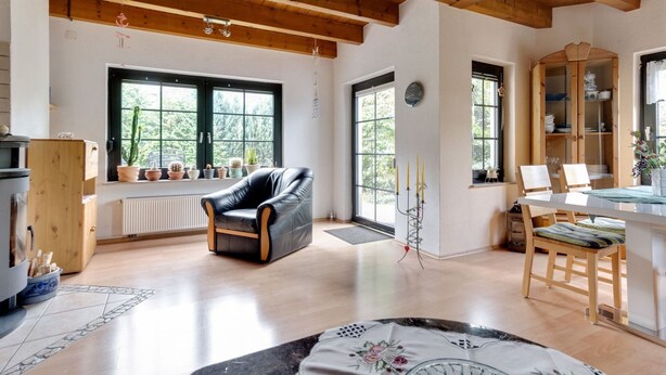 Amplia sala de estar con techo de madera, ventanas grandes, un sillón de cuero negro, una mesa de comedor con sillas y un aparador con vajilla.