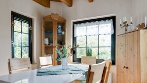 Un comedor con una mesa blanca, sillas de madera, un armario y una ventana con vistas a la vegetación.