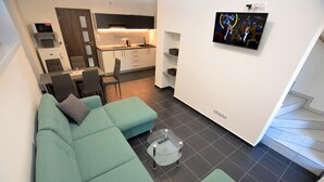 A modern living room with a sectional sofa, a glass coffee table, and a kitchen area in the background. - Cozy Forest Adventure Stay (Zelezna Ruda)