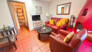 A living room with a red sofa, a coffee table, a TV, and a bookshelf. - Casita I - 2 Bed, 2 Bath (Santa Fe)