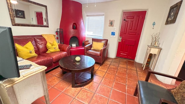A living room with a red sofa, a brown leather armchair, a coffee table, and a red door. - Casita I - 2 Bed, 2 Bath (Santa Fe)