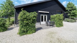 Een modern zwart gebouw met een grindpad, een deur en een klein terras met een tafel en stoelen.