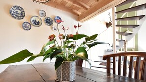 Een eettafel met een potplant, houten stoelen en blauw-witte borden aan de muur.
