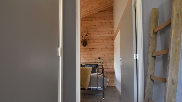 Een hal met een houten plafond en een bed met hoofdeinde tegen een muur.